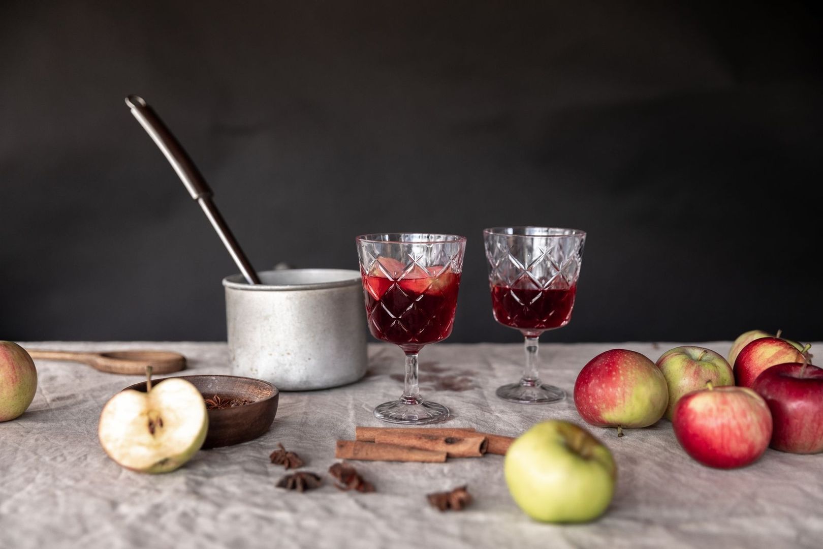 Zwei Gläser mit rotem Apfelgetränk, Äpfel und Gewürze auf einem Tisch